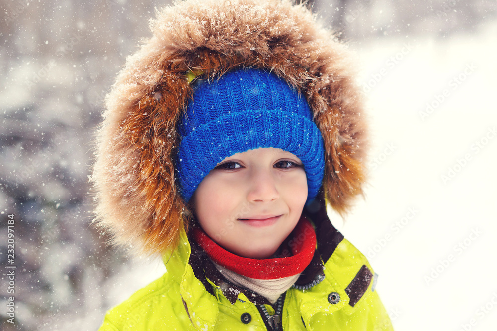 Cute child boy in winter clothes outdoors. Portrait of happy little boy  playing under snow. Happy kid on walk during snowfall. Winter holidays.  Winter kids fashion. Happy and healthy childhood. Stock Photo
