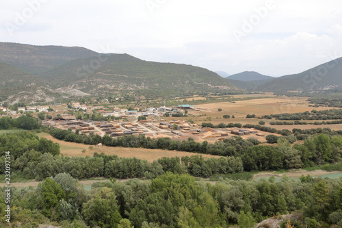 A landscape of rocky mountains and crop fields with Santa Maria y la Peña rural town, as seen from Mallos de Riglos, in the Pyrenees, Aragon, Spain