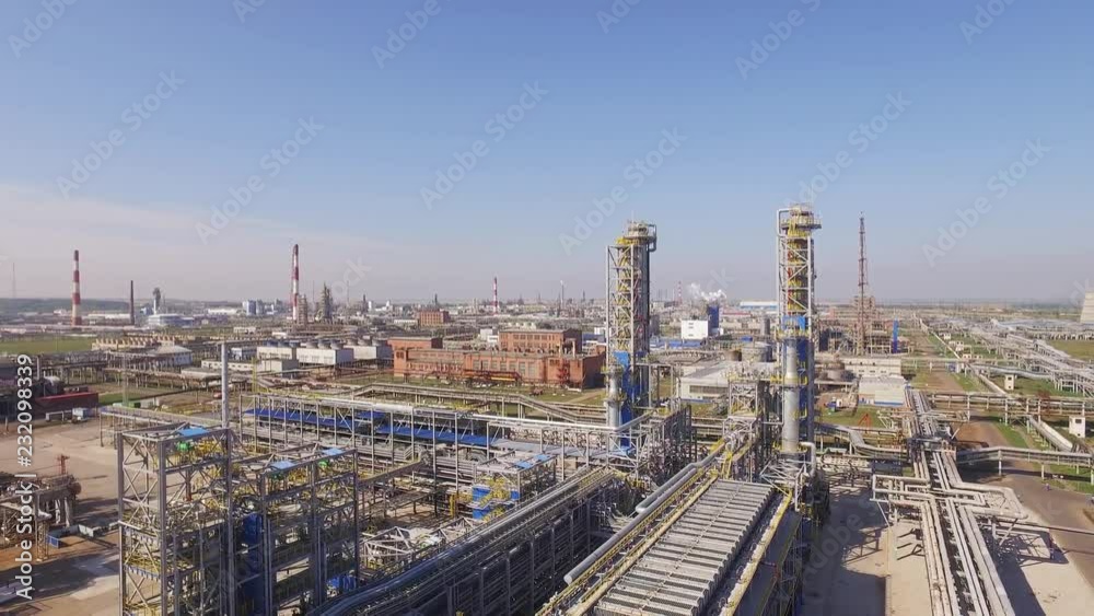 Giant oil refinery in rural areas on a summer sunny day with a clear blue sky. Red and white pipes, a huge territory among agricultural crops - Aerial view. Giant oil refinery in rural areas on a summer sunny day with a clear blue sky. Red and white pipes, a huge territory among agricultural crops - Aerial view.