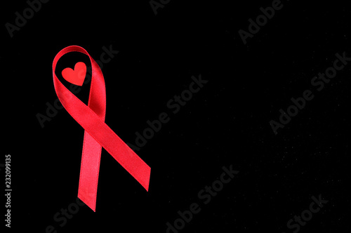 World AIDS Day concept, red ribbon with small red heart on black and red background, an international day dedicated to raising awareness of the AIDS