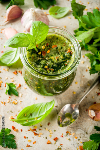 Argentinian traditional food, raw homemade green Chimichurri salsa or sauce woth parsley, garlic, basil leaves, hot pepper and spices, light stone table copy space photo