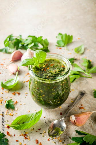 Argentinian traditional food, raw homemade green Chimichurri salsa or sauce woth parsley, garlic, basil leaves, hot pepper and spices, light stone table copy space