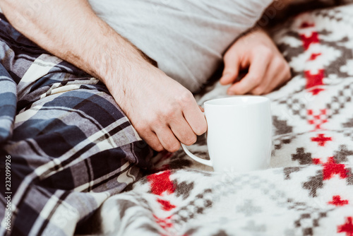 cropped image of man sitting in bed with coffee cup at home