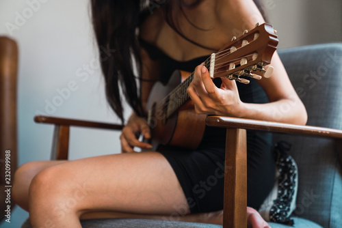Young woman sitting on armchair at home playing guitar