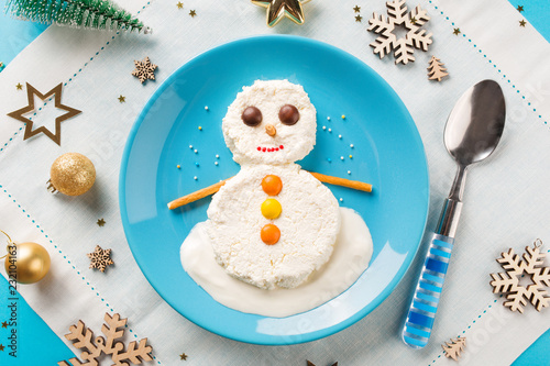 Fun food idea for kids. Christmas children's Breakfast: snowman of cottage cheese on a blue plate.
