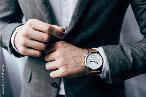 partial view of businessman with watch buttoning up jacket photo