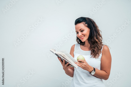 Young woman reading a book and eating apple on isolated background.
