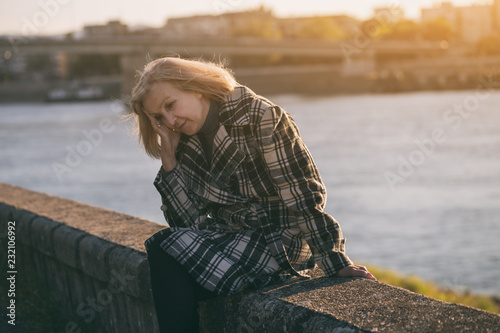 Senior woman having headache while sitting by the river.