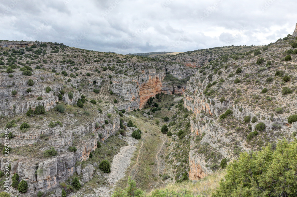 The Barranco de la Hoz Seca (Dry Defile Gully) canyon, with scarps, bushes and red rocks, in a cloudy atumn, in the Jaraba rural town, Aragon, Spain