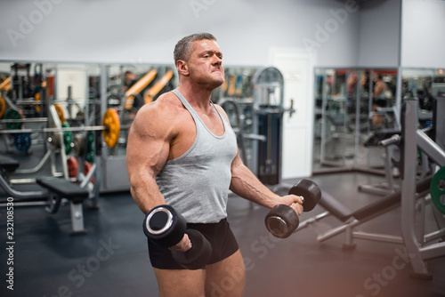 athletic man trains in the gym. Training biceps with a dumbbells