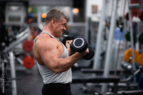 athletic man trains in the gym. Training biceps with a dumbbells