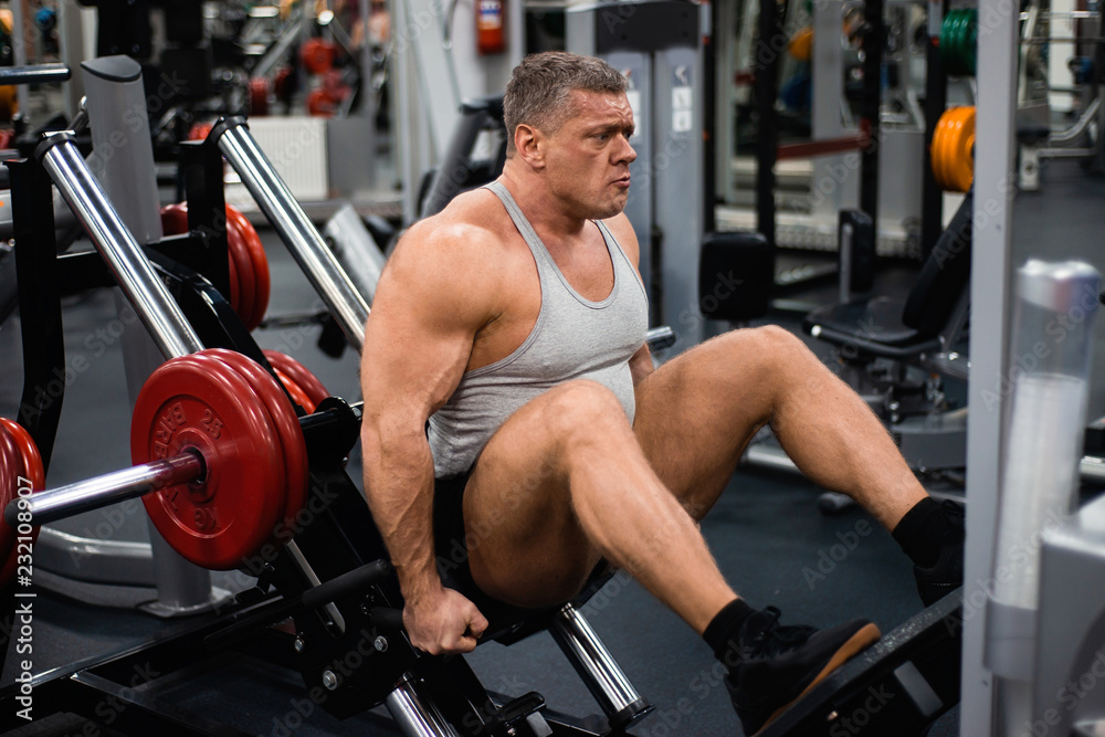 muscular man trains his legs in the gym. Health and fitness concept muscular man trains his legs in the gym. Health and fitness concept