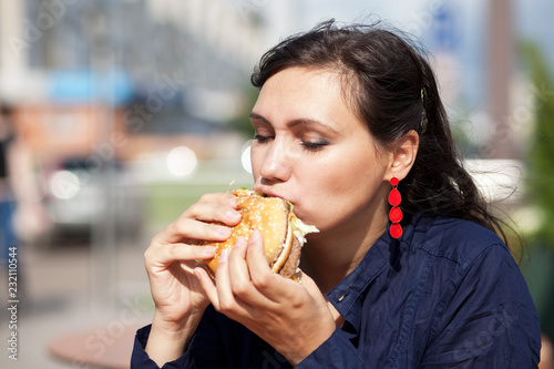 Beautiful girl with an appetite eating a hamburger on the street photo