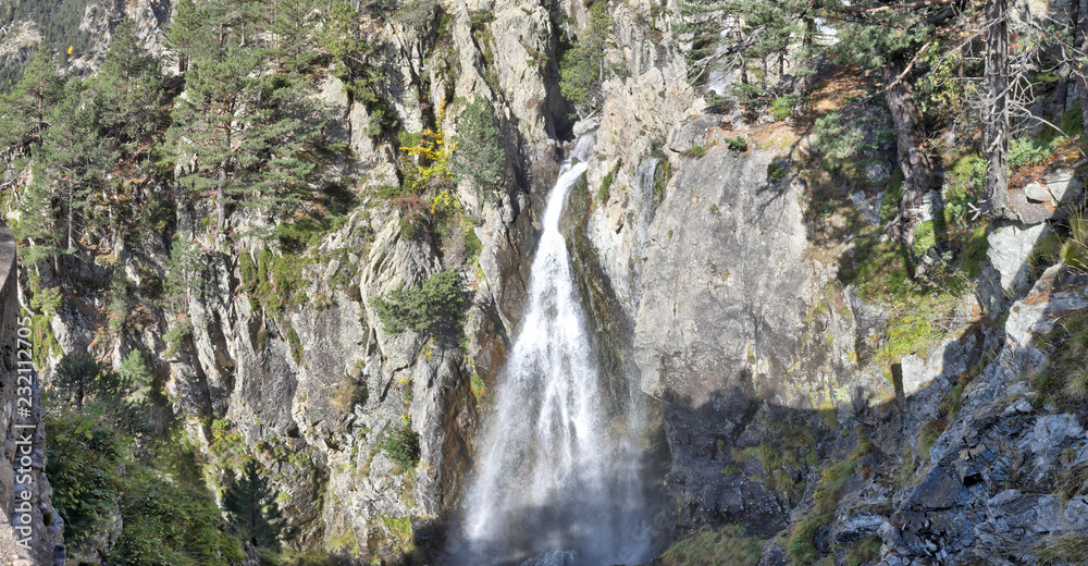 A Caldarès river waterfall during a sunny autumn in the firs and pine trees forest of the rocky mountains of Panticosa, Aragon Pyrenees, Spain A Caldarès river waterfall during a sunny autumn in the firs and pine trees forest of the rocky mountains of Panticosa, Aragon Pyrenees, Spain