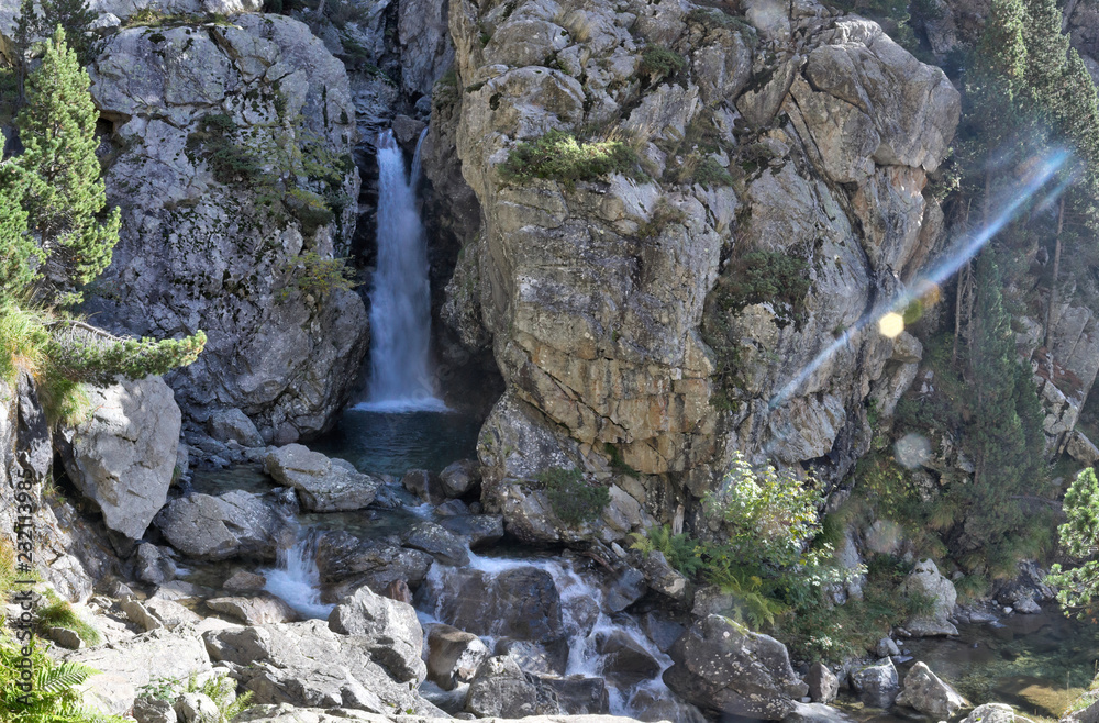 A Caldarès river waterfall during a sunny autumn in the firs and pine trees forest of the rocky mountains of Panticosa, Aragon Pyrenees, Spain A Caldarès river waterfall during a sunny autumn in the firs and pine trees forest of the rocky mountains of Panticosa, Aragon Pyrenees, Spain