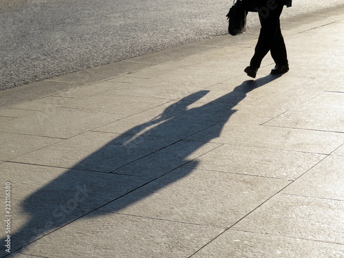 Silhouette of person walking down the street, long shadow on pavement. Man with briefcase, concept for official, businessman, politician, career growth photo