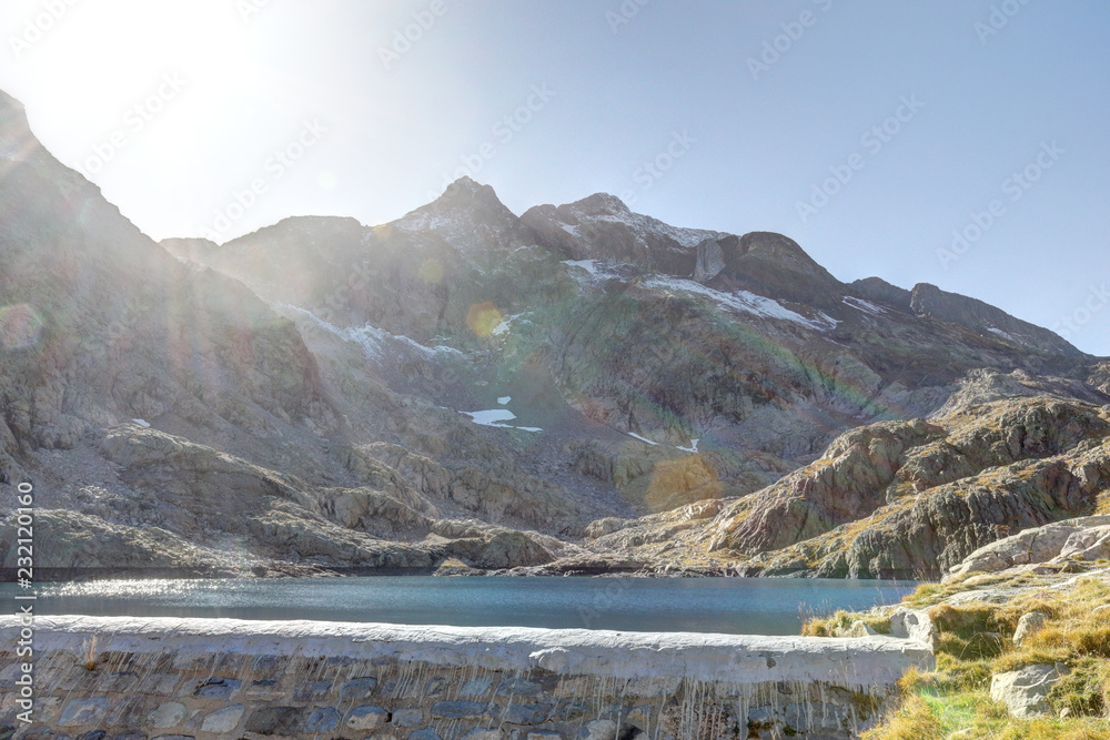 The lower Blue Lake (Ibon Azul) dam, among barren rocky mountains with snow and a blue sky in a sunny autumn, in Panticosa, Aragon Pyrenees, Spain