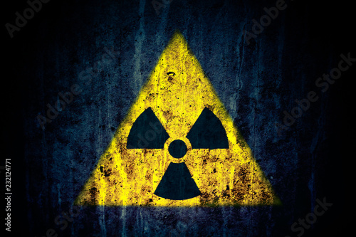 Radioactive (ionizing radiation) danger yellow symbol over a massive cracked concrete wall with and dark rustic grunge blueish texture background.