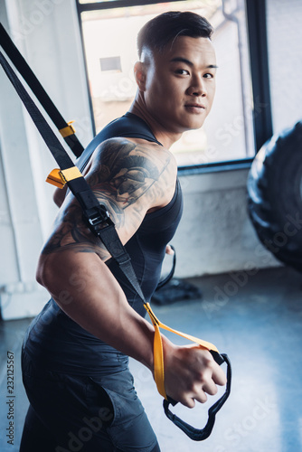 concentrated young asian muscular sportsman training with resistance bands in gym