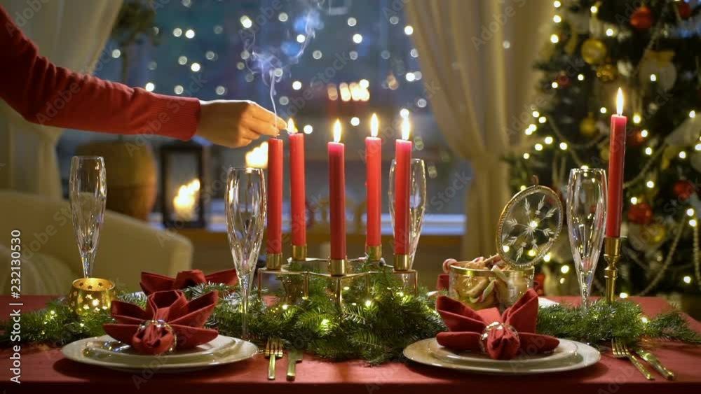 Fale hand lights christmas candles. Festival red table setting with garland and Christmas tree in the background Slow motion