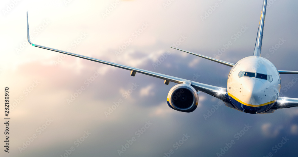 Close up of commercial passenger airplane flying above the clouds at sunset