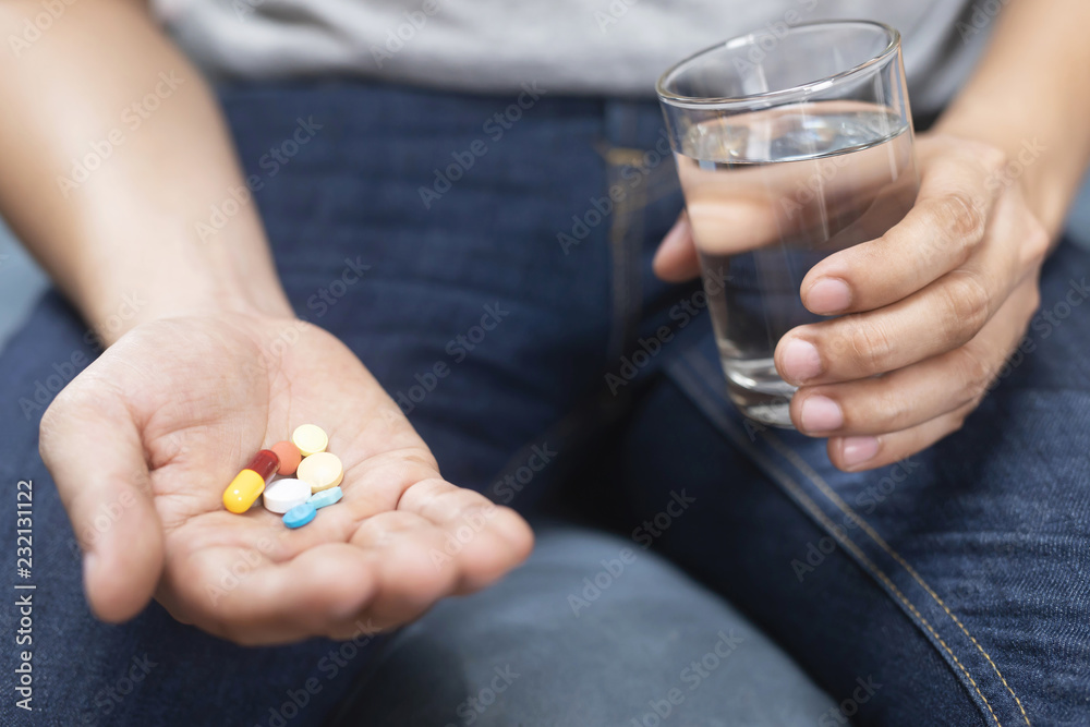 close up hand man taking multiple colors pills take a medicine in hand holding a cup glass of drinking water. Stop drug use Taking Medication health care medical concept close up hand man taking multiple colors pills take a medicine in hand holding a cup glass of drinking water. Stop drug use Taking Medication health care medical concept
