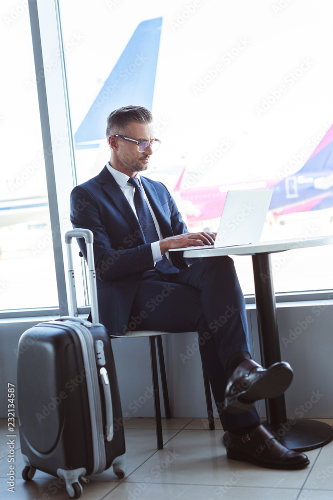 adult businessman in glasses typing on laptop at table in airport adult businessman in glasses typing on laptop at table in airport