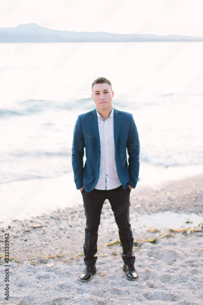 The portrait of attractive groom in a suit standing against the background of Garda lake. Italy