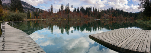 fall color forest and foliage panorama landscape surround an idyllic mountain lake in the Alps of Switzerland on a late autumn day with reflections in the water with a wooden boardwalk in the foregrou photo