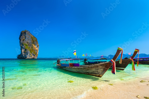 Wooden longtailed boats on a sandy beach in the crystal clear turquoise water of the Adaman Sea near the picturesque limestone rock island under a blue sky. Poda Island, AO Nang, Krabi, Thailand.
