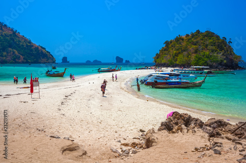 Tropical island at high tide. Vacationers walk on the white hot sand, on the shore at anchor are transport boats to carry customers. Tup Island, AO Nang, Krabi, Thailand - Februrary 2014. photo