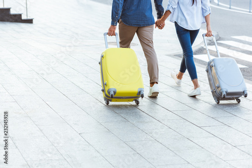 cropped view of couple of tourists holding hands and pulling their luggage