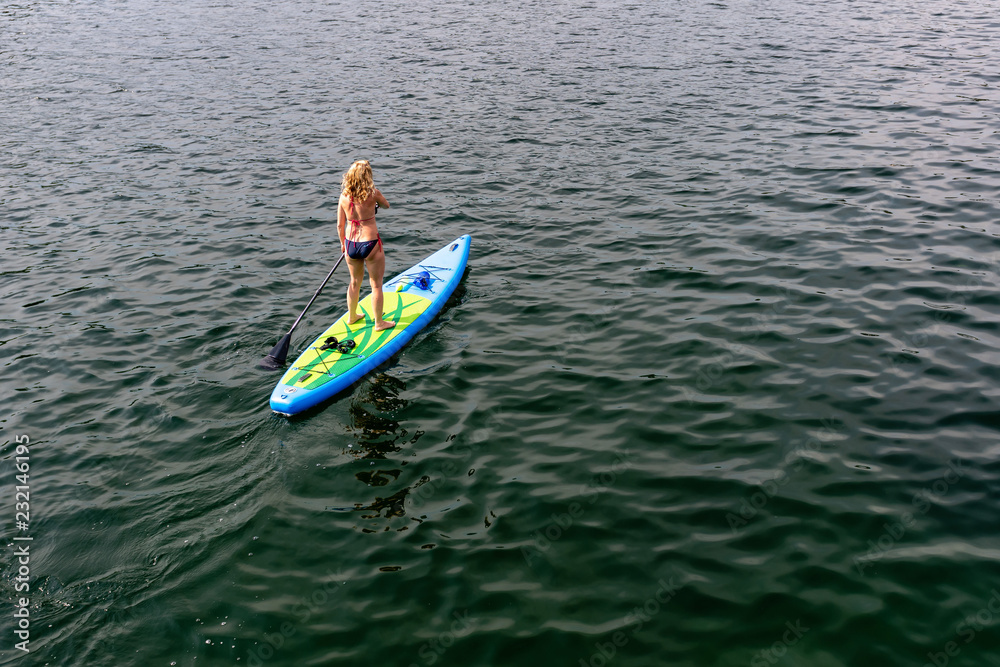 Young Woman on Paddle Board at the lake. SUP. View from back.
