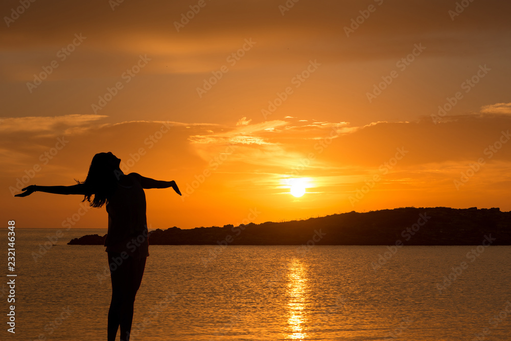 Dawn in the sea with the silhouette of a happy young woman
