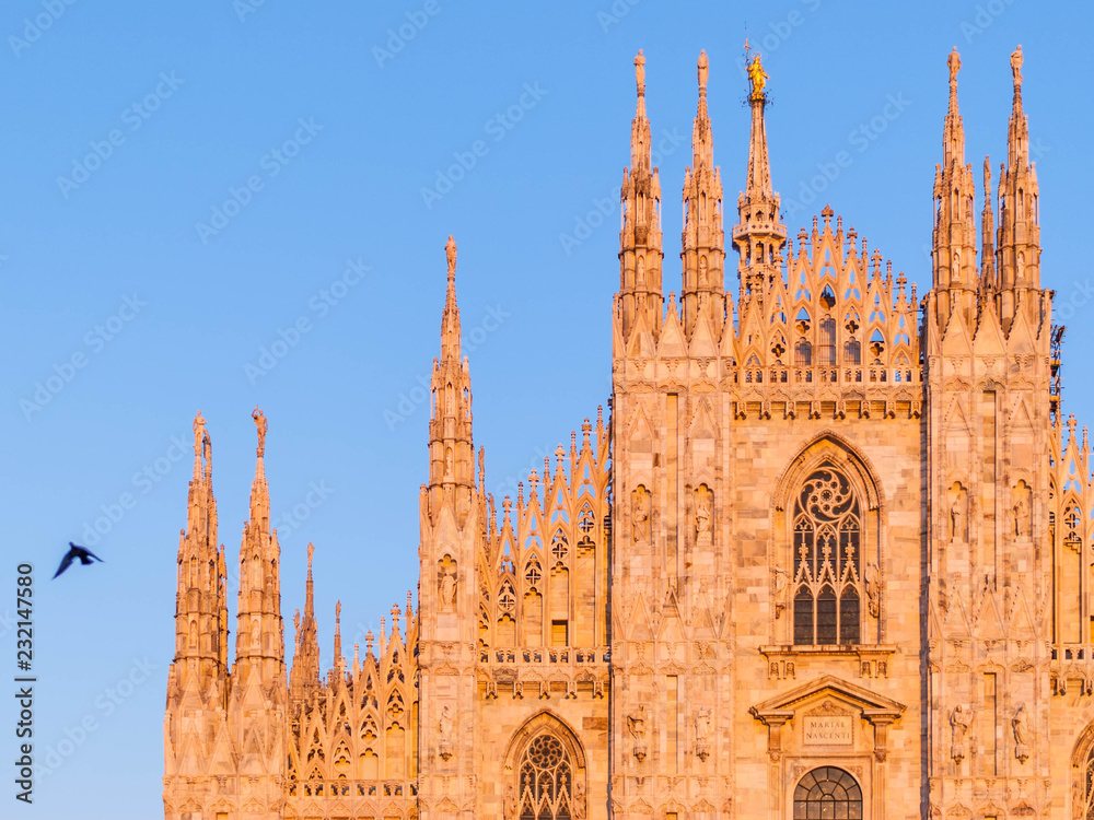 Fragment of the facade of Cathedral Duomo di Milano lit by the setting sun at the golden hour against the clear blue sky, Milan, Italy