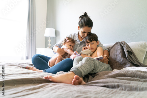 Mother and sons reading book in bedroom
