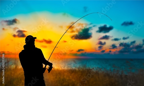 Tablou canvas Silhouette of fishing man on coast of sunset sea