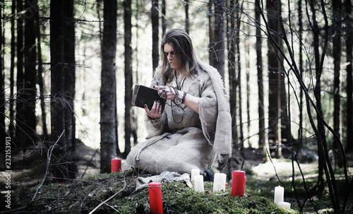 Fairy magician. A sorcerer with a glass sphere, a magical spell and a ritual. Elder with a staff and a cross in the forest. Black and white magic. A spell in an old book.
