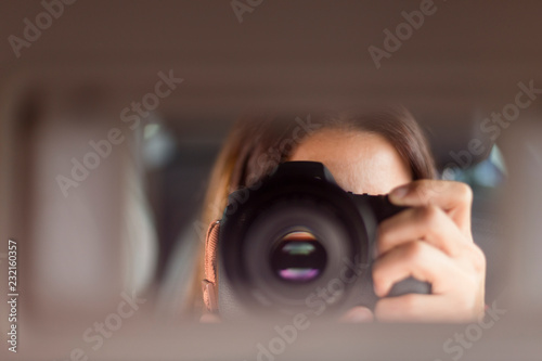 young woman sitting on copilot seat taking a picture with relfex camera in rear mirror inside the car, daytime. travel concept photo