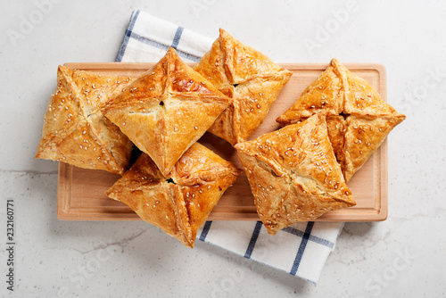 Puff pastry squares filled with potato, cheese and spinach on light gray stone table.top view
