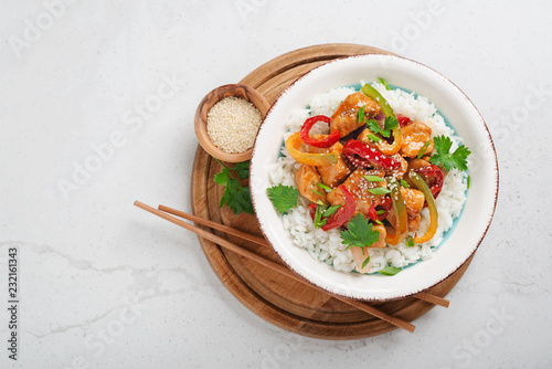 Stir-fry with chicken meat, vegetables and rice in bowl on light gray stone background.