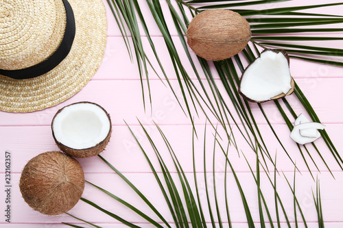 Ripe coconuts with palm leafs and hat on pink wooden table