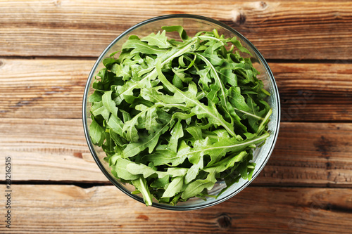 Green arugula leafs in glass bowl on brown wooden table