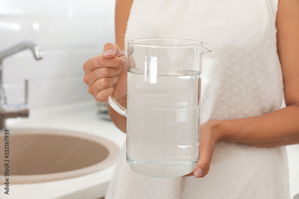 Woman holding glass jug with water in kitchen, closeup Woman holding glass jug with water in kitchen, closeup