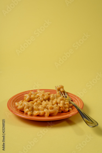 Side view of macaroni and cheese on an orange plate with fork with a yellow background. photo