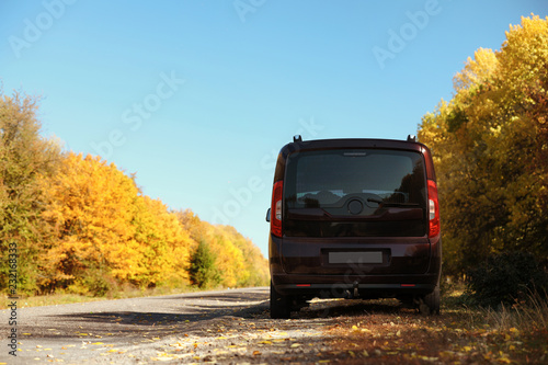 Car parked on country road near autumn forest. Space for text