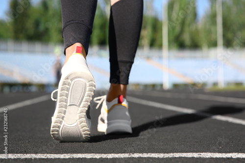 Sporty woman running at stadium on sunny morning, focus on legs