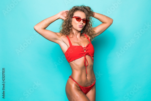 Beautiful young curly woman in a sunglasses and red swimsuit on a green background