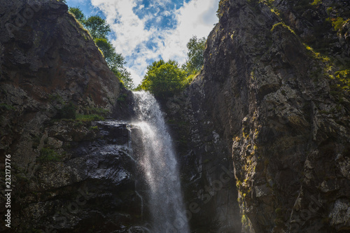A high waterfall with white splashes of water descends from the mountain and sparkles in the sun. Attraction of Georgia Gveleti waterfall © Ольга Симонова