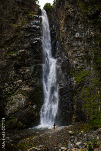 A high waterfall with white splashes of water descends from the mountain and sparkles in the sun. Attraction of Georgia Gveleti waterfall